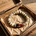 Bone bead bracelet with turquoise and red inlay bands and a red-brown dzi bead, in an open wooden box