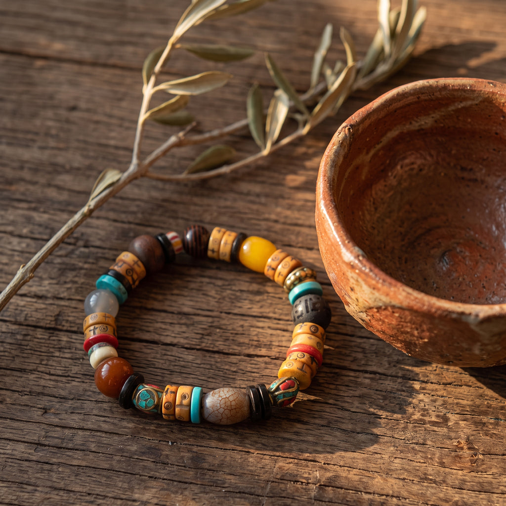Mixed-bead bracelet of carved yak bone, turquoise, agate and a crackled gray barrel bead beside a clay bowl on old wood