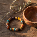 Mixed-bead bracelet of carved yak bone, turquoise, agate and a crackled gray barrel bead beside a clay bowl on old wood