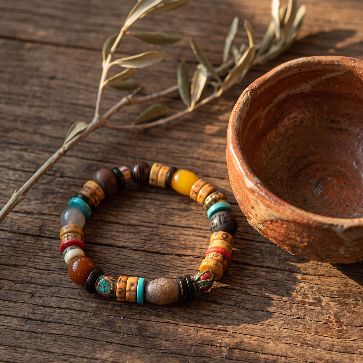 Mixed-bead bracelet of carved yak bone, turquoise, agate and a crackled gray barrel bead beside a clay bowl on old wood