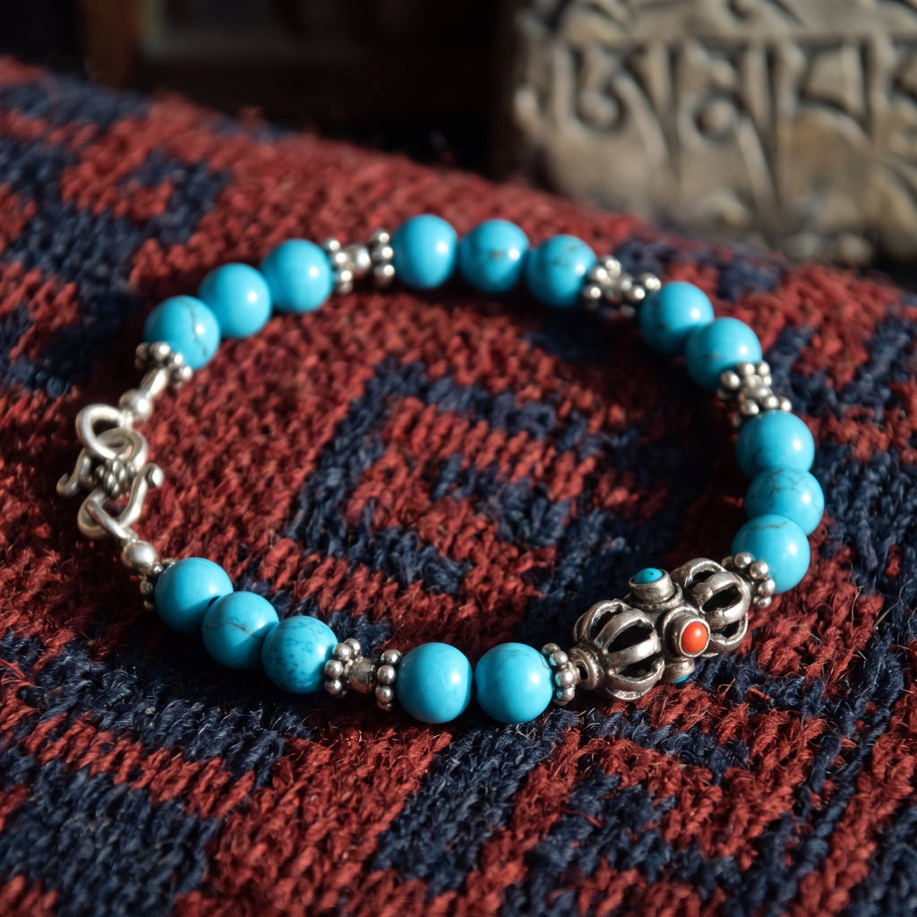 Turquoise bead bracelet with a silver vajra and small silver spacers on a red and blue woven rug