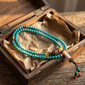 Turquoise 108-bead mala with metal inlaid beads, yellow and red accents and a white guru bead in an open wooden box