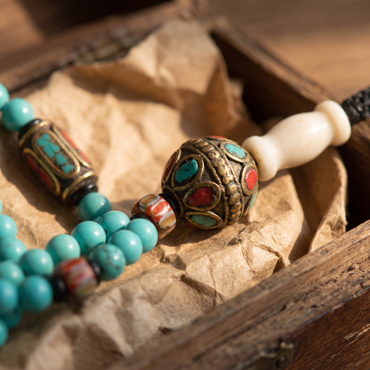 Detail of a round metal bead inlaid with turquoise and red stones beside a white bone guru bead