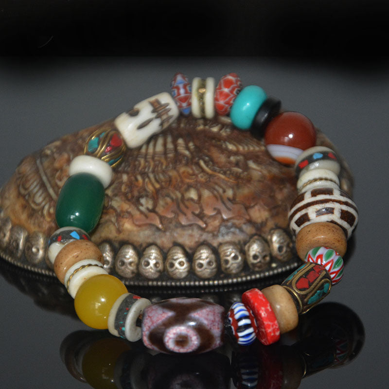 Mixed-bead bracelet with a three-eyed dzi, green and yellow agate, glass and carved bone beads on a carved dish