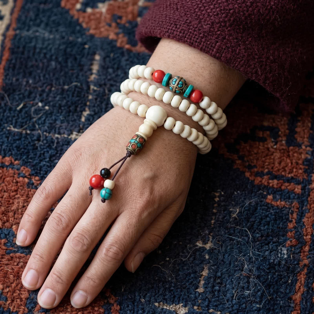 Yak bone mala wrapped three times around a wrist as a bracelet, red, turquoise and brass counter beads on top