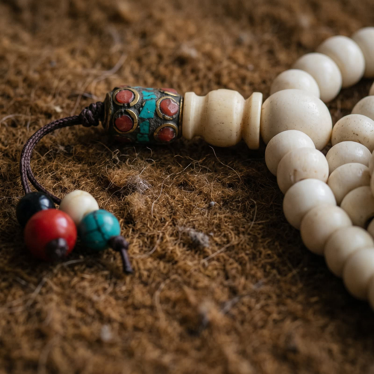 Close-up of the bone guru bead, stupa bead and brass tube inlaid with red stones and turquoise, with black, red, white and turquoise end beads