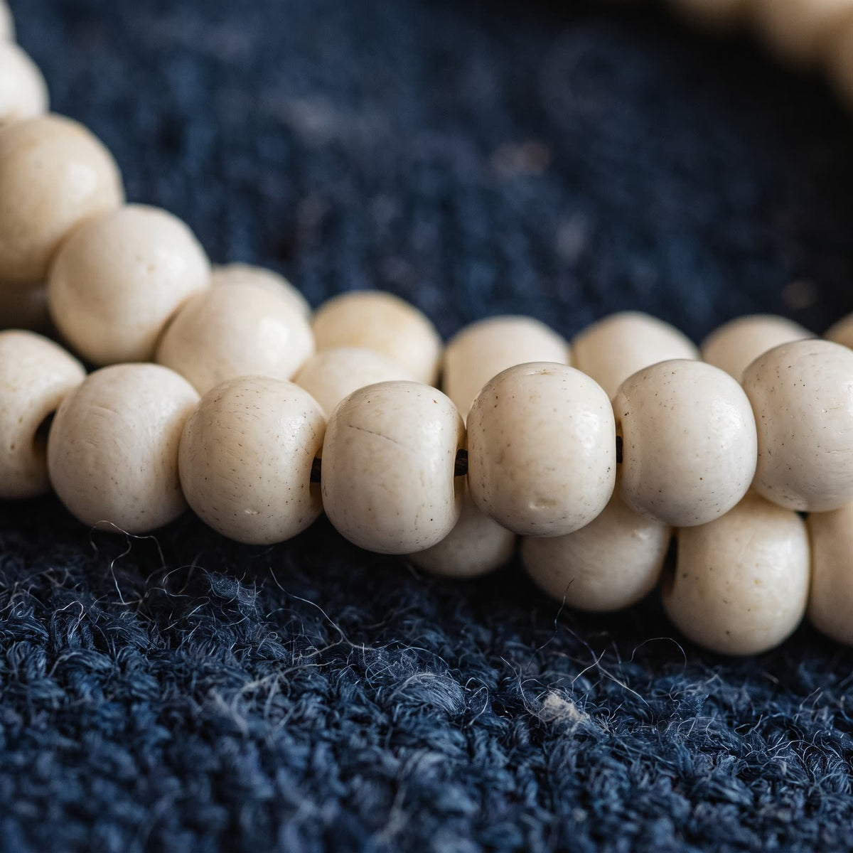 Macro of ivory yak bone beads showing natural flecks, pores and fine grain on indigo wool