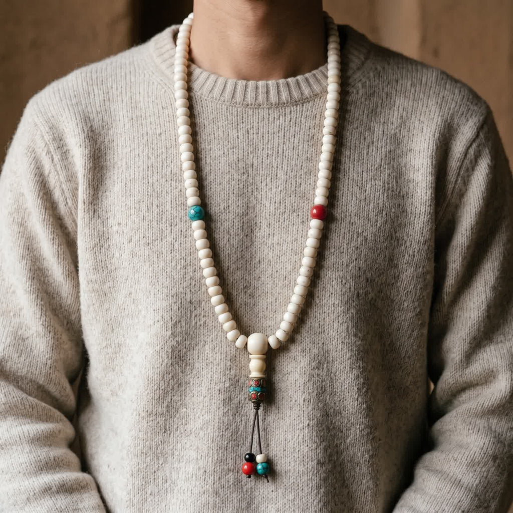 Yak bone mala worn long over an oatmeal wool sweater, guru bead and inlaid brass tube at the centre