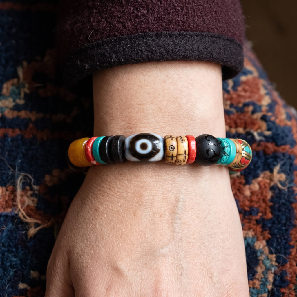 Black-and-white eye dzi bracelet worn on a woman's wrist below a maroon wool sleeve