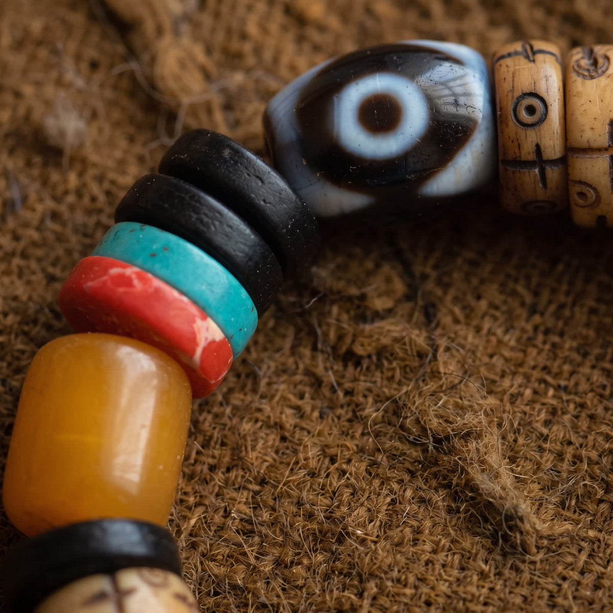 Close-up of the eye dzi bead between black, turquoise and red discs and a honey-yellow barrel bead