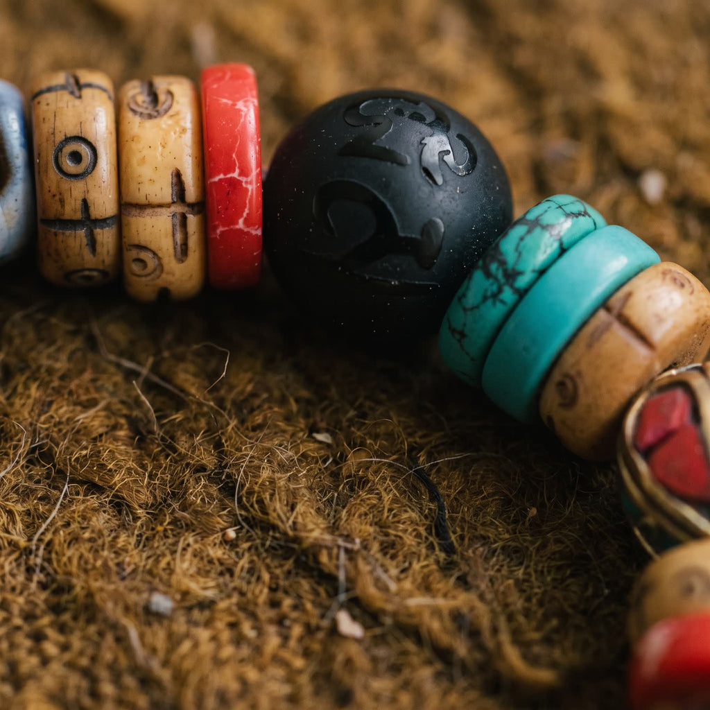 Close-up of carved yak bone discs, a red disc and a matte black bead carved with a mantra glyph