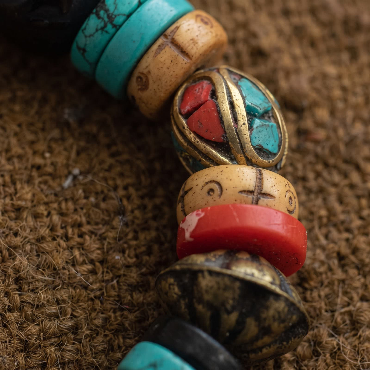 Close-up of a brass bead inlaid with red and turquoise chips and an embossed brass saucer bead