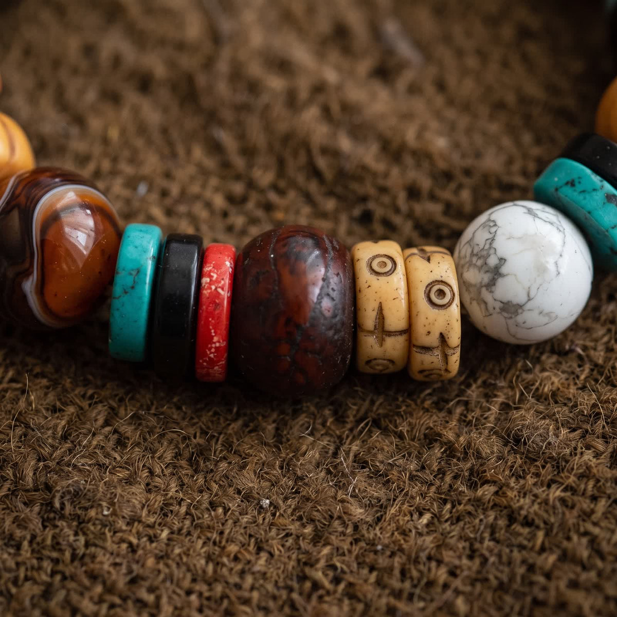 Close-up of a banded agate bead, a dark red-brown round bead, carved bone discs and a white veined bead