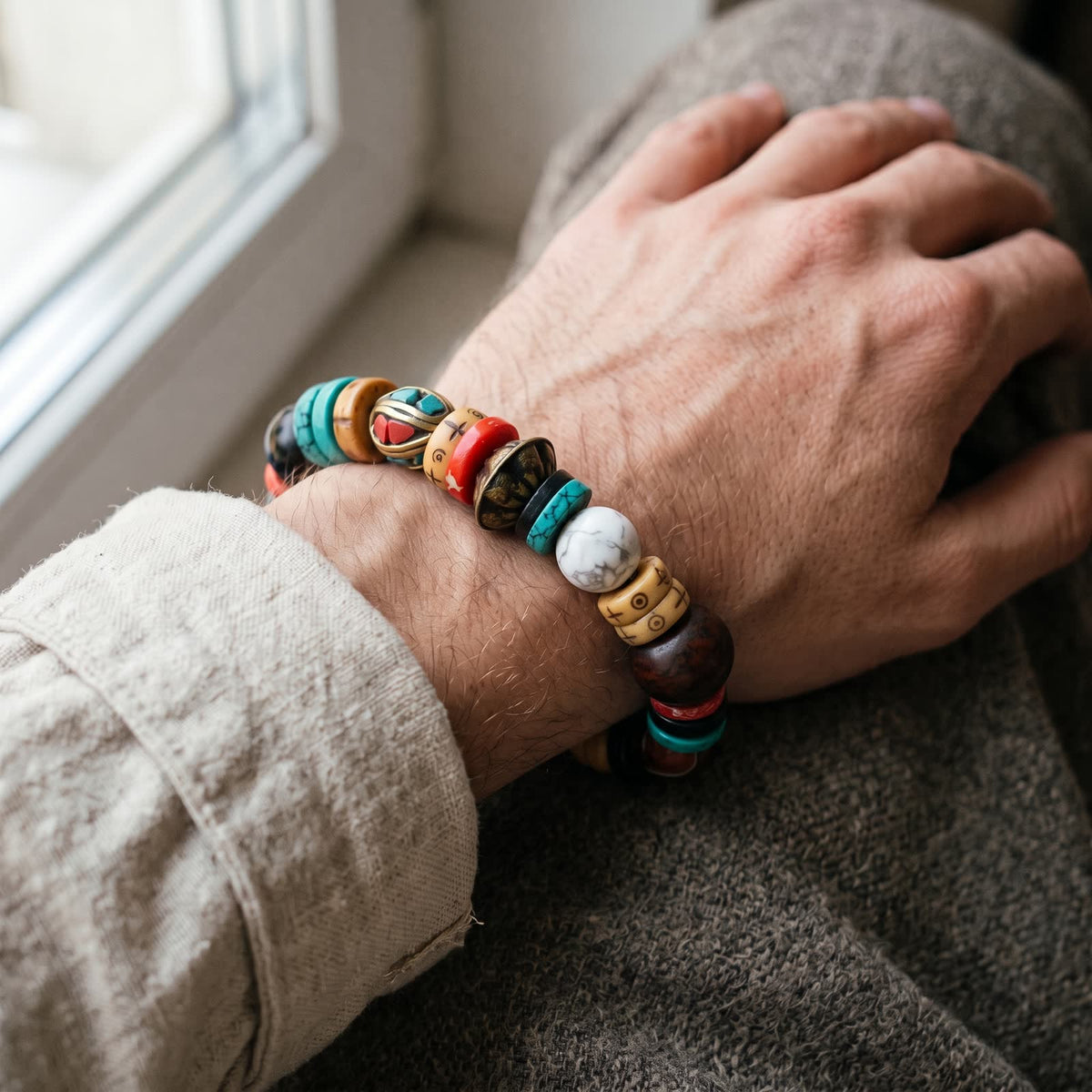 Bracelet worn on a man's wrist showing the white veined bead and brass beads, linen sleeve rolled back
