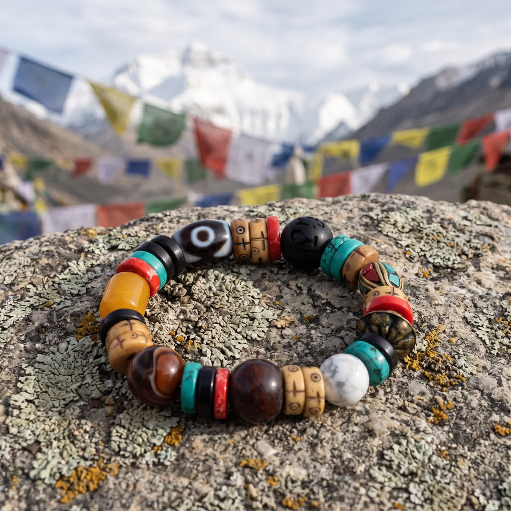 Dzi bracelet on a lichen-covered stone with prayer flags and snow peaks blurred behind