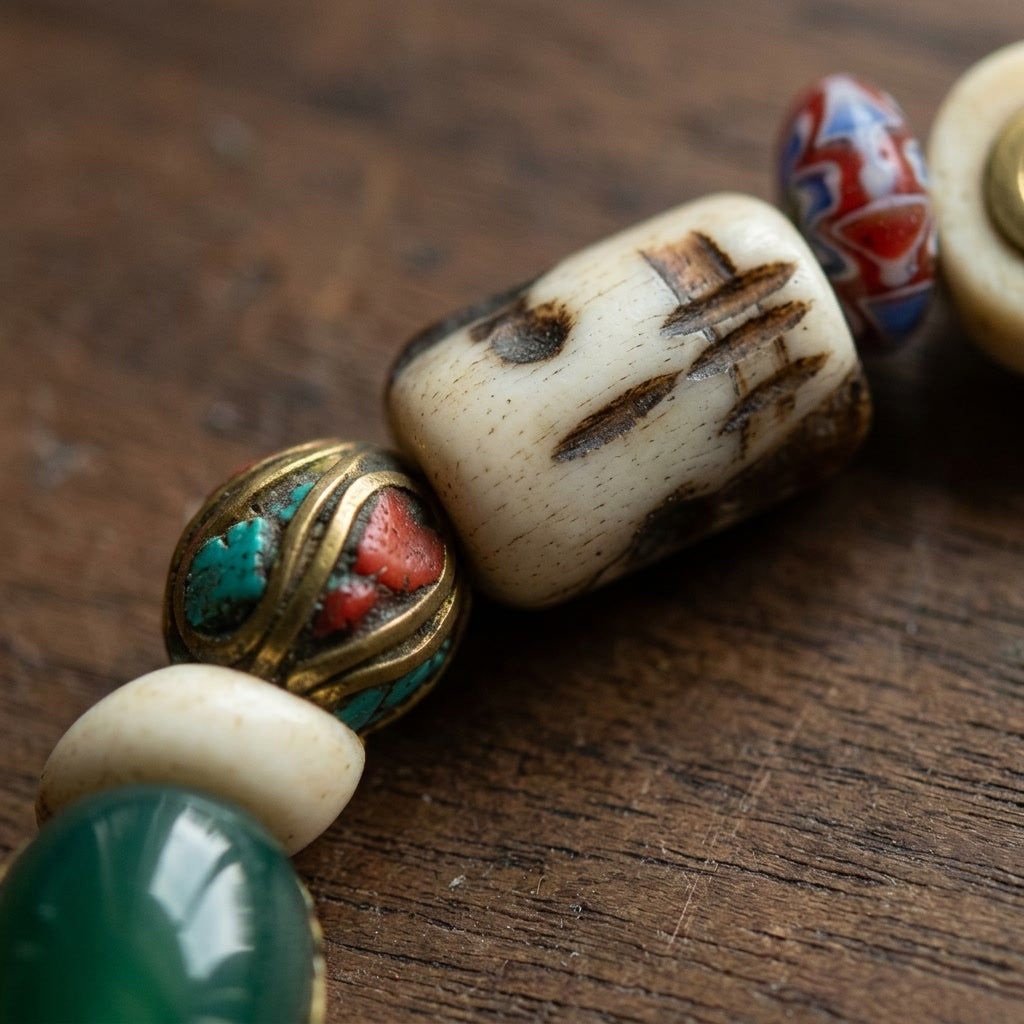 Close-up of a brass bead inlaid with turquoise and red stone beside a carved bone barrel bead and green agate