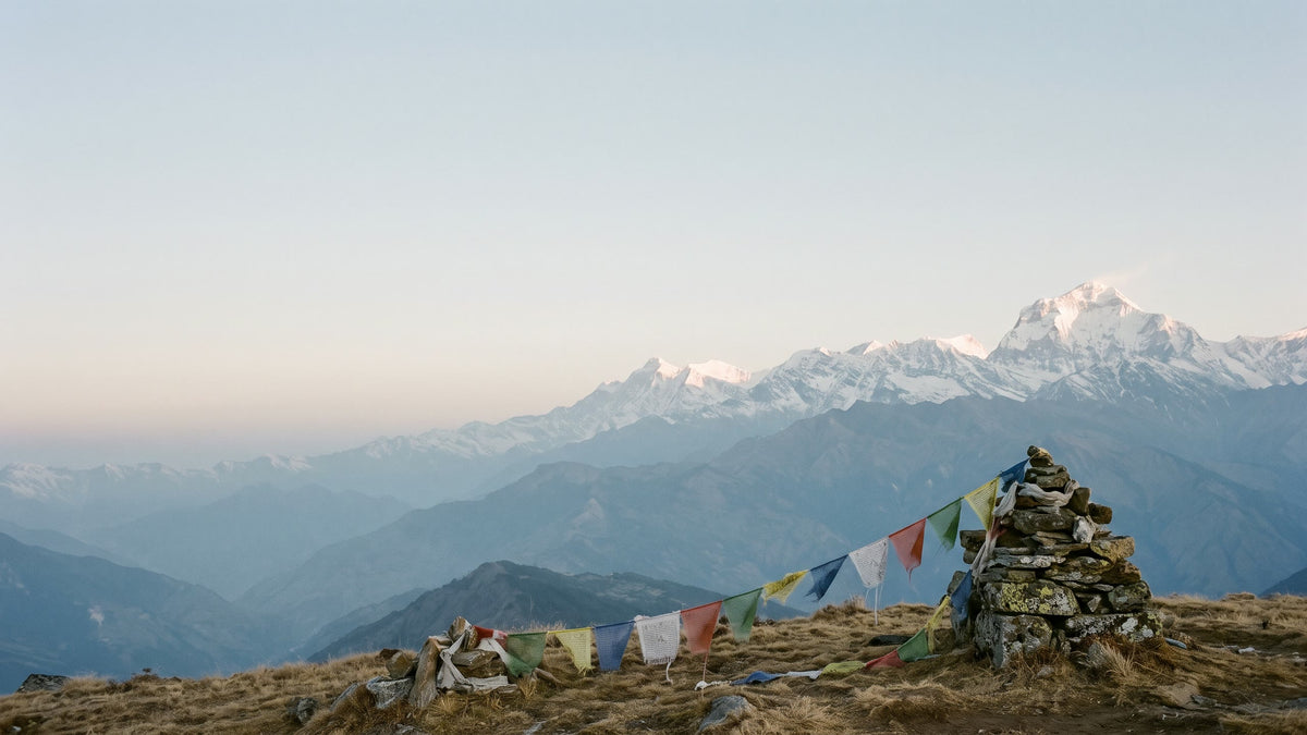 Faded prayer flags on a stone cairn on a high grassy pass, a Himalayan snow range in first light beyond