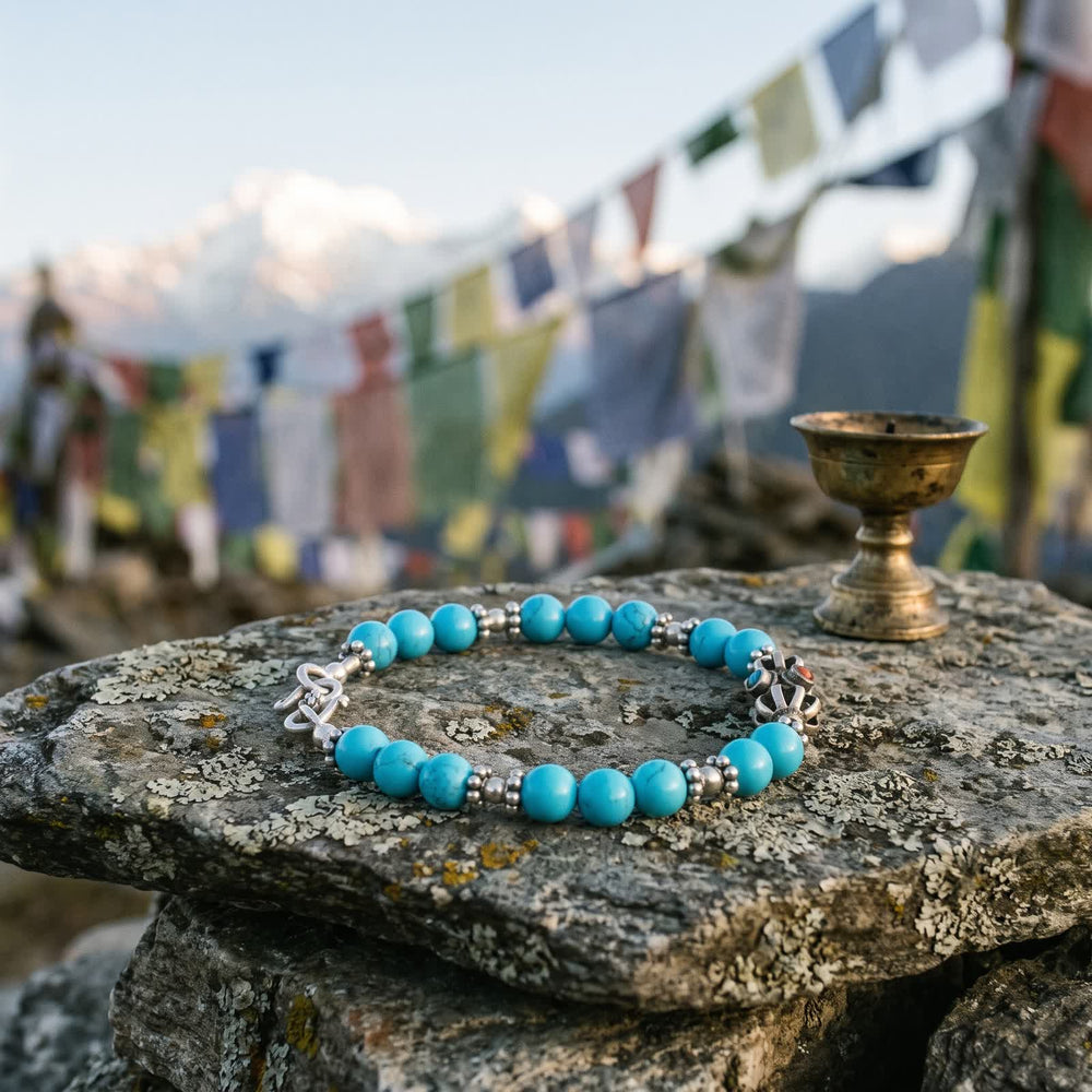 Blue turquoise and silver vajra bracelet on a lichen-covered stone at a mountain pass, prayer flags and snowy peaks behind