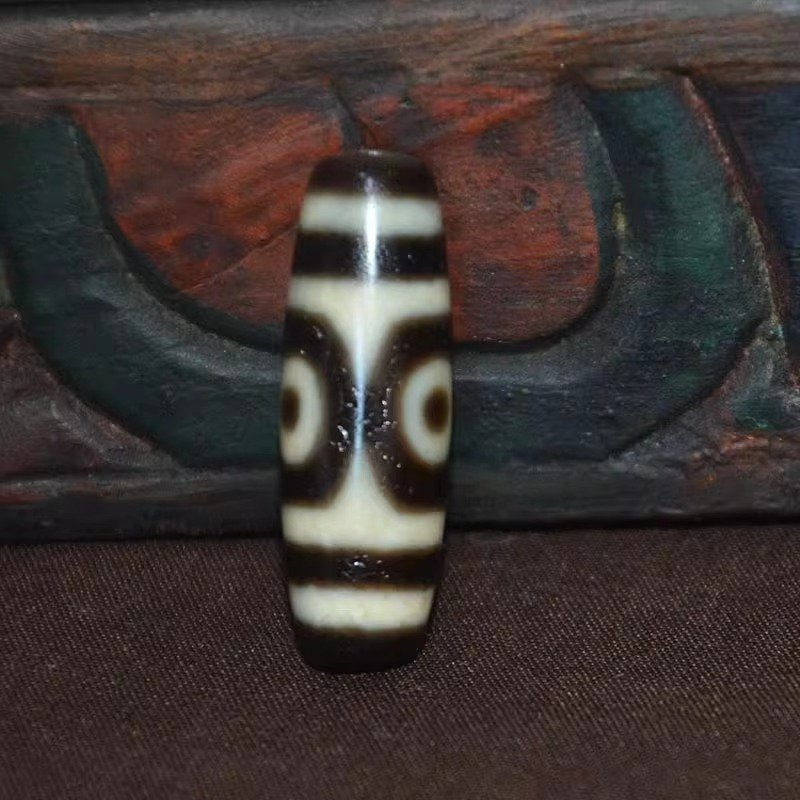 Real photo of the two-eyed agate dzi bead standing upright against carved wood