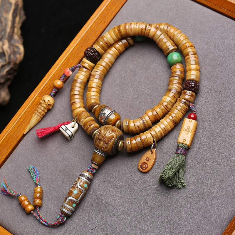 Supplier photo of the yak bone 108 disc mala with carved bone guru bead and bone dzi-pattern bead on a grey tray