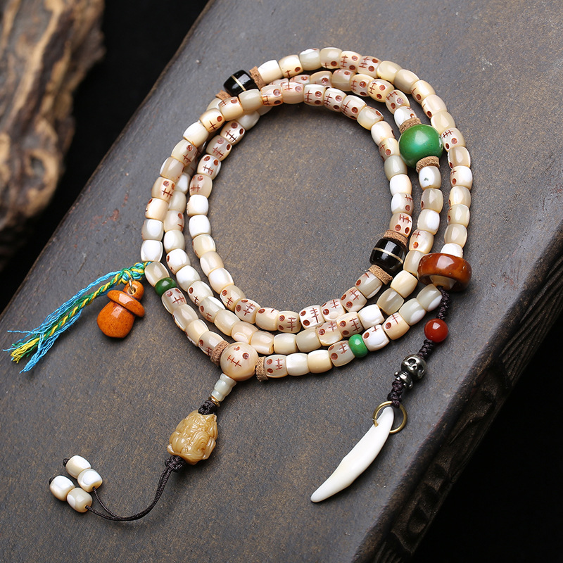 Supplier photo of the fish bone 108 mala with carved skull beads laid flat on dark stone